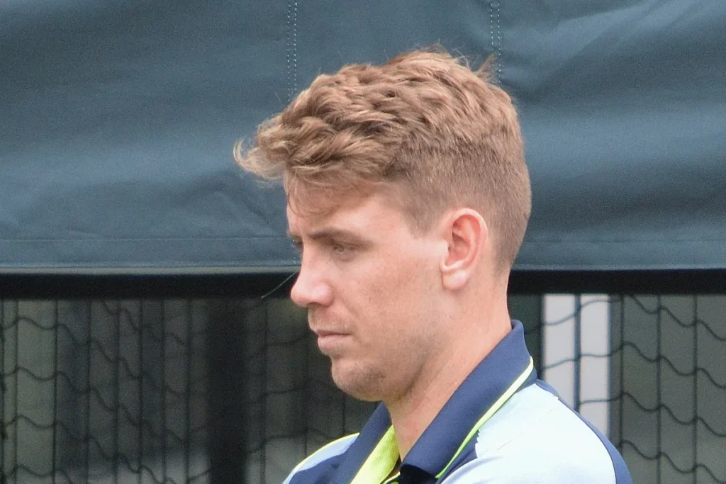 Head-and-shoulders side view of Australian all-rounder Cameron Green with tousled sandy hair, in a navy training shirt in front of practice nets.