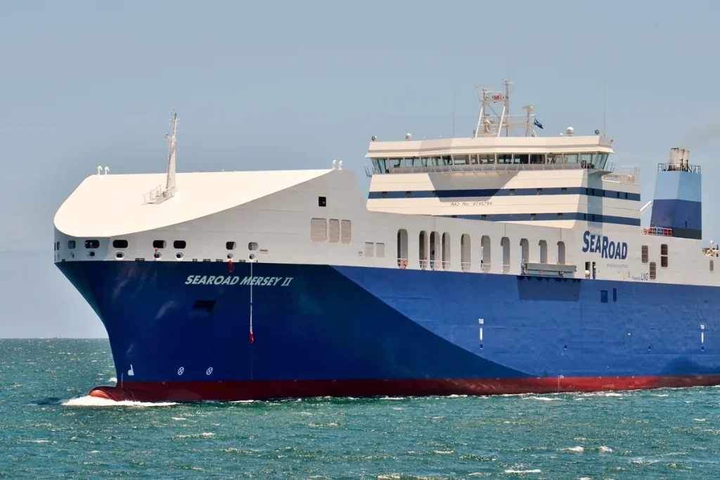A large blue-hulled, white-topped cargo ferry with SEAROAD on its side moving through green water under a hazy sky.