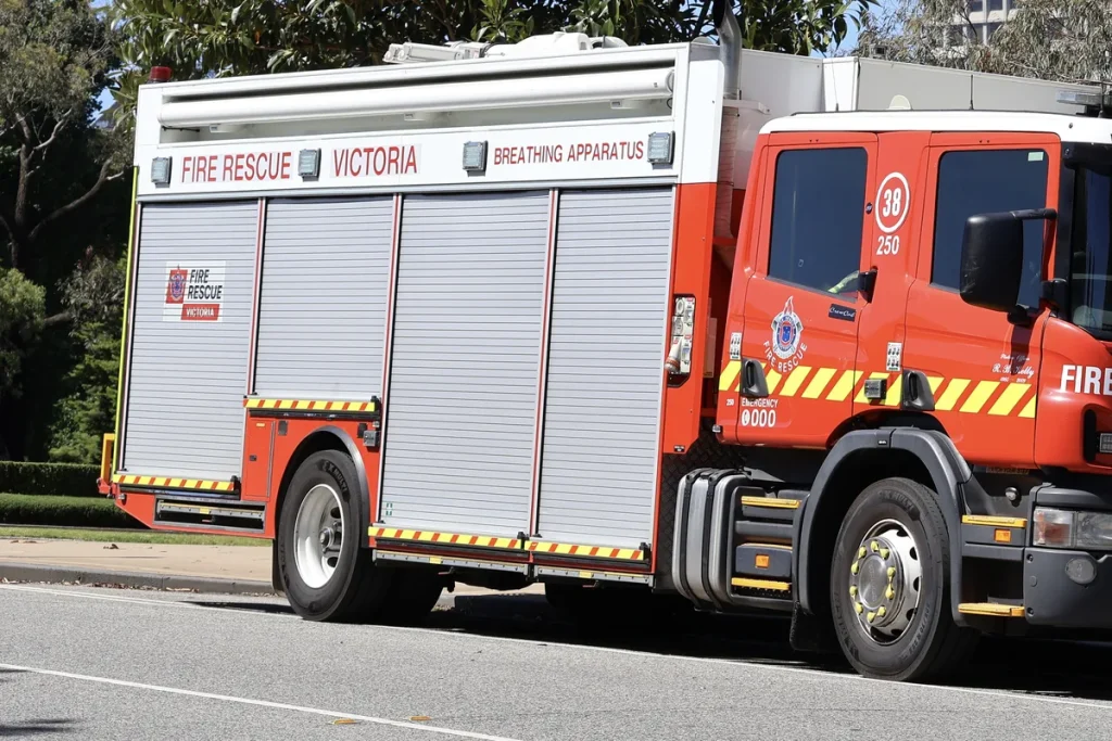 The side of a red and silver Fire Rescue Victoria fire truck with roller-door lockers marked Breathing Apparatus, parked on a sunny Melbourne street.
