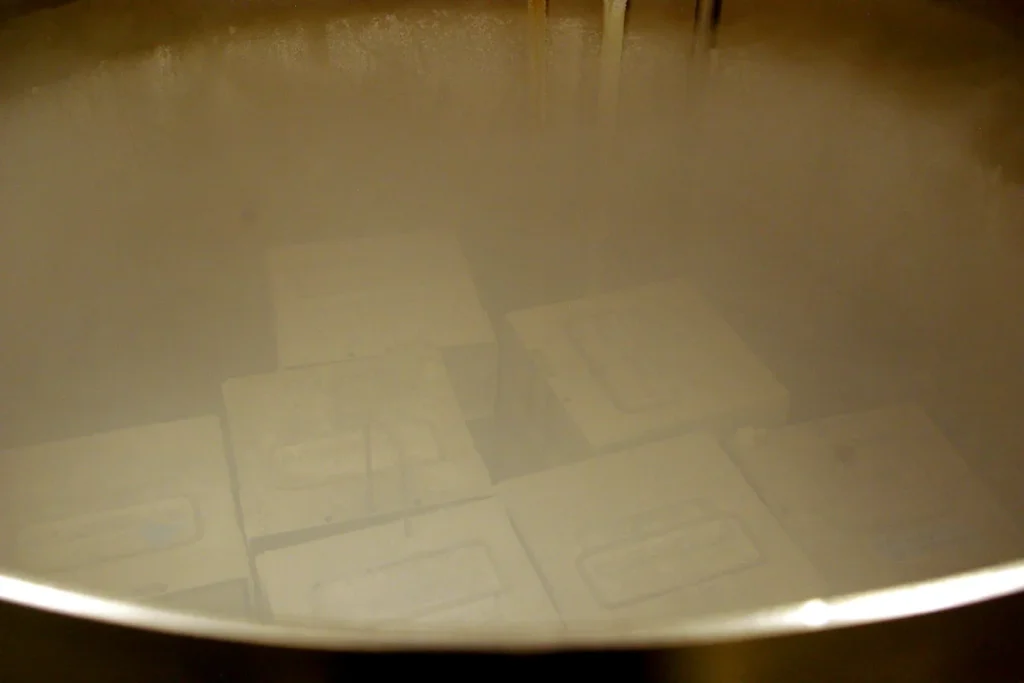 Frosted metal storage boxes stacked inside a round cryogenic tank, partly hidden by cold white vapour.