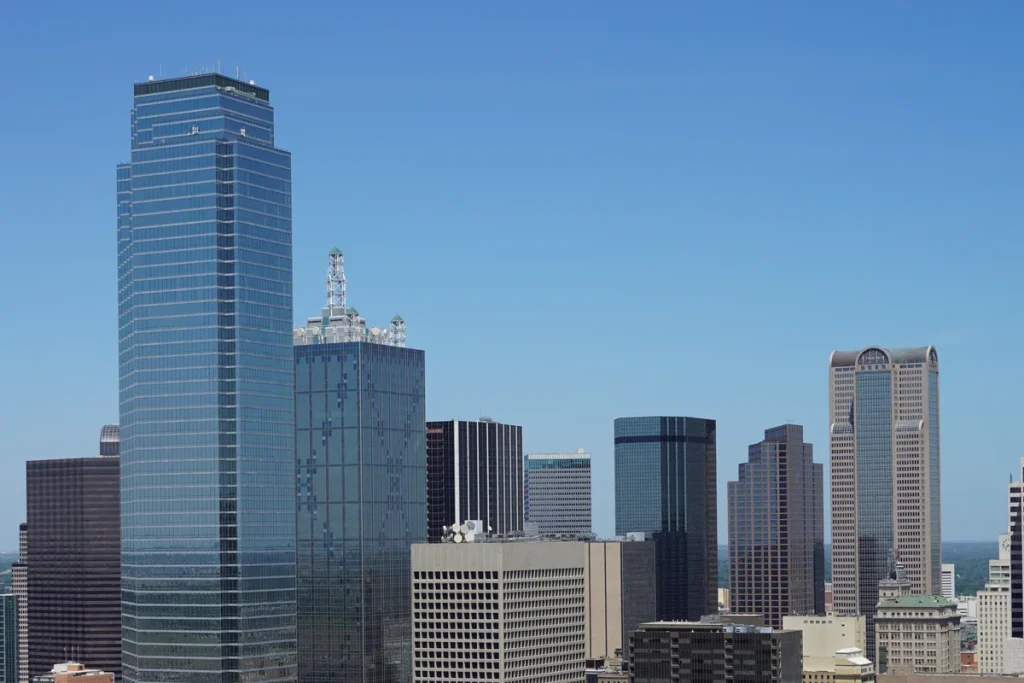 Downtown Dallas skyline of glass and stone towers under a clear blue sky, seen from above.