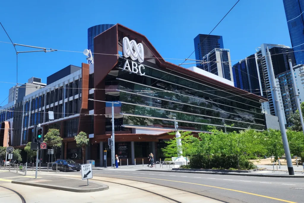 Modern ABC building in Southbank, Melbourne, with a rust-coloured frame and the ABC logo on its corner, tram lines in the street in front.