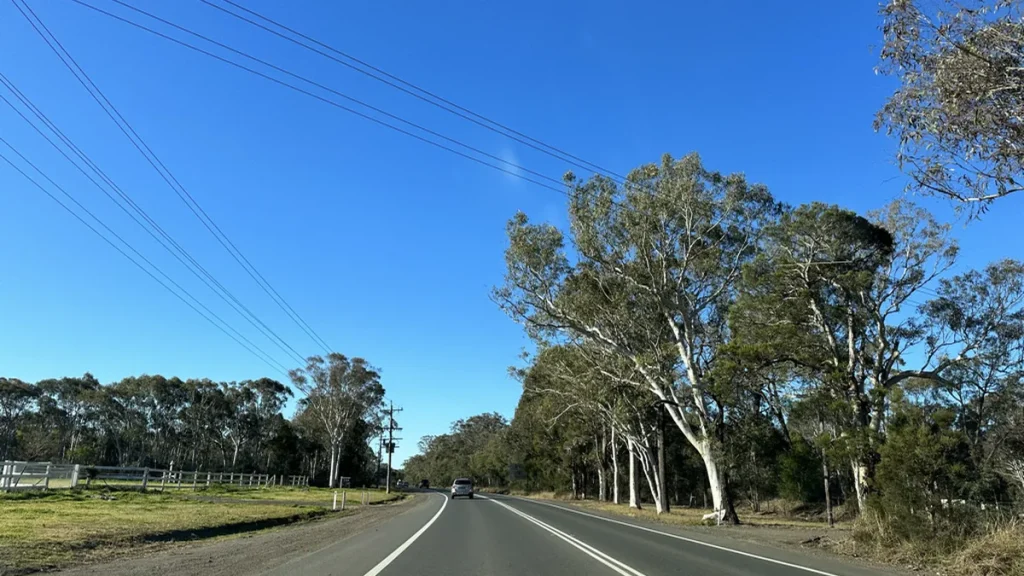 A view along The Northern Road at the Londonderry and Llandilo boundary in western Sydney, with a car ahead on the two-lane road, eucalypts on both sides, powerlines overhead and paddocks to the left; photographed in 2023. Illustrative, not the property or the scene of the seizure.