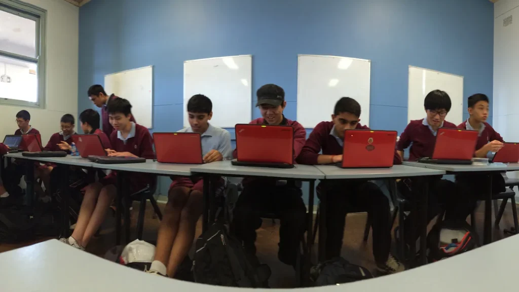 Students in maroon school uniform using red laptops at long desks in a classroom at Sydney Technical High School in New South Wales, seen in a wide view, with whiteboards on the blue wall behind them; photographed in 2014. Illustrative, not from the PISA 2025 testing.