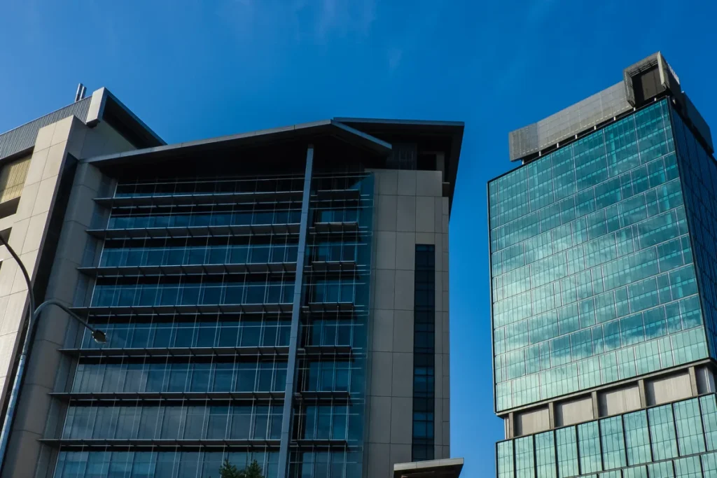 The Brisbane Magistrates Court building with its glass facade and sun louvres beside a neighbouring glass office tower against a deep blue sky.
