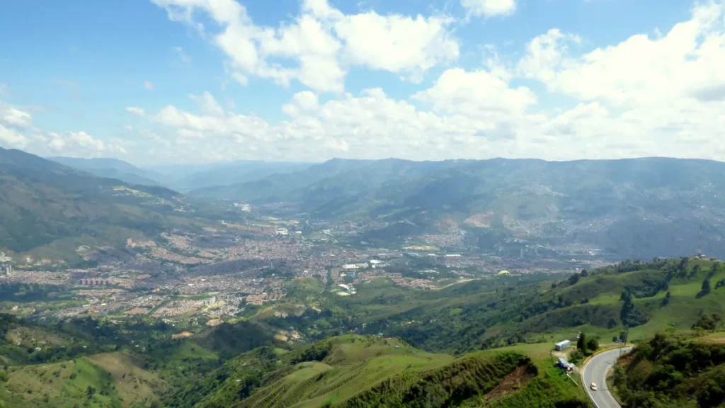 Aerial view over the Aburrá Valley near Medellín in Colombia, with the built-up areas of Bello and Copacabana spread across the valley floor below green mountains and a blue sky, and a road curving through the hills at the lower right; photographed in December 2014. A general view of the place, not from the detention reported in the article.