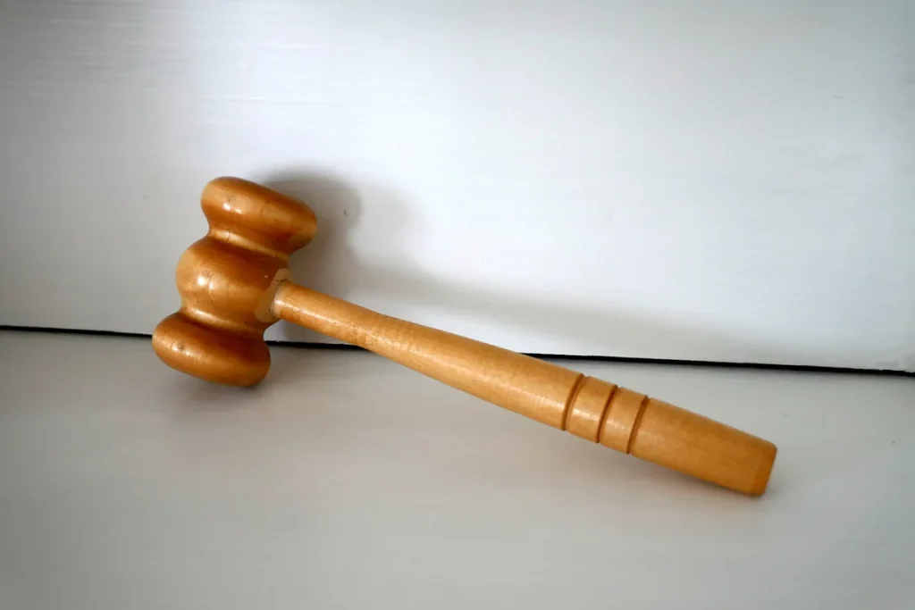 A plain wooden gavel resting on a white surface against a white wall.